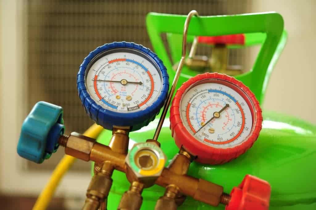 Close-up of HVAC manifold gauges with blue and red dials attached to a green refrigerant tank, showing pressure readings.