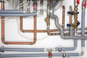 A network of copper and grey PVC pipes with valves and connectors mounted on a white wall, part of a plumbing or heating system.
