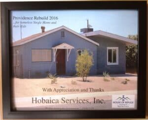 A framed certificate thanking Hobaica Services, Inc. for supporting Providence Rebuild 2016 for homeless single moms and their kids, with a photo of a blue house and a Bible quote.