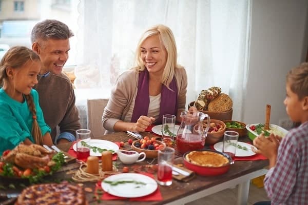 Four people sit around a table enjoying a meal together, with various dishes, bread, and drinks arranged on the table.