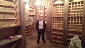 %Focuskw% | Hobaica Services A person stands in a room with wooden wine racks, shelves, and a rustic brick wall. Warm ceiling lights illuminate the space.