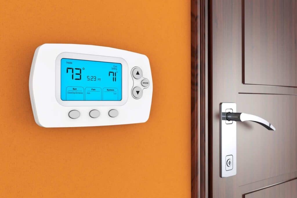 Digital thermostat on an orange wall displays 73°F and time 5:23 PM, next to a closed wooden door with a silver handle.