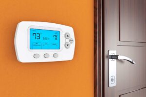 Digital thermostat on an orange wall displays 73°F and time 5:23 PM, next to a closed wooden door with a silver handle.