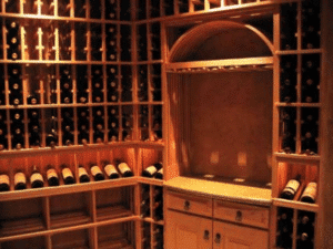 A wine cellar with wooden racks holding dozens of wine bottles, a built-in countertop, drawers, and warm lighting.