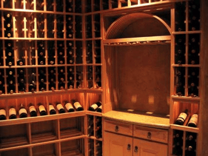 A wine cellar with wooden racks holding dozens of wine bottles, a built-in countertop, drawers, and warm lighting.
