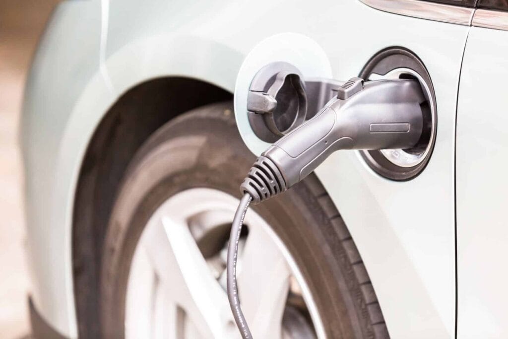 Close-up of an electric vehicle being charged, showing the charging cable plugged into the port near the rear wheel.