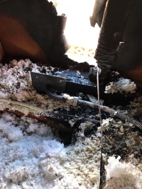 Burnt insulation and charred electrical wiring are visible in an attic space, with significant fire damage to the surrounding materials.
