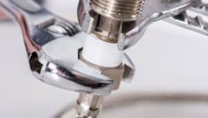 An adjustable wrench tightens a metal pipe fitting wrapped with white Teflon tape.