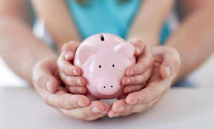 Adult and child hands holding a pink piggy bank together, symbolizing saving money and financial guidance.