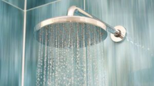 A modern round showerhead mounted on a tiled bathroom wall, spraying water downward.