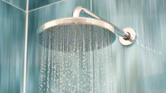 A modern round showerhead mounted on a tiled bathroom wall, spraying water downward.