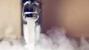 Close-up of a faucet with hot water running, producing visible steam or vapor around the stream.