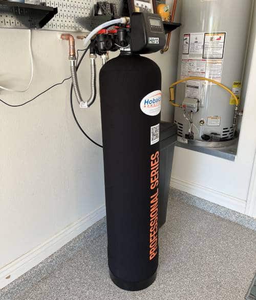 A black water softener tank labeled "Professional Series" stands next to a water heater in a garage or utility room.